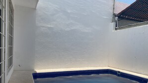 Una pequeña piscina cercada, con borde de azulejos azules, rodeada por un muro blanco y una reja de metal.