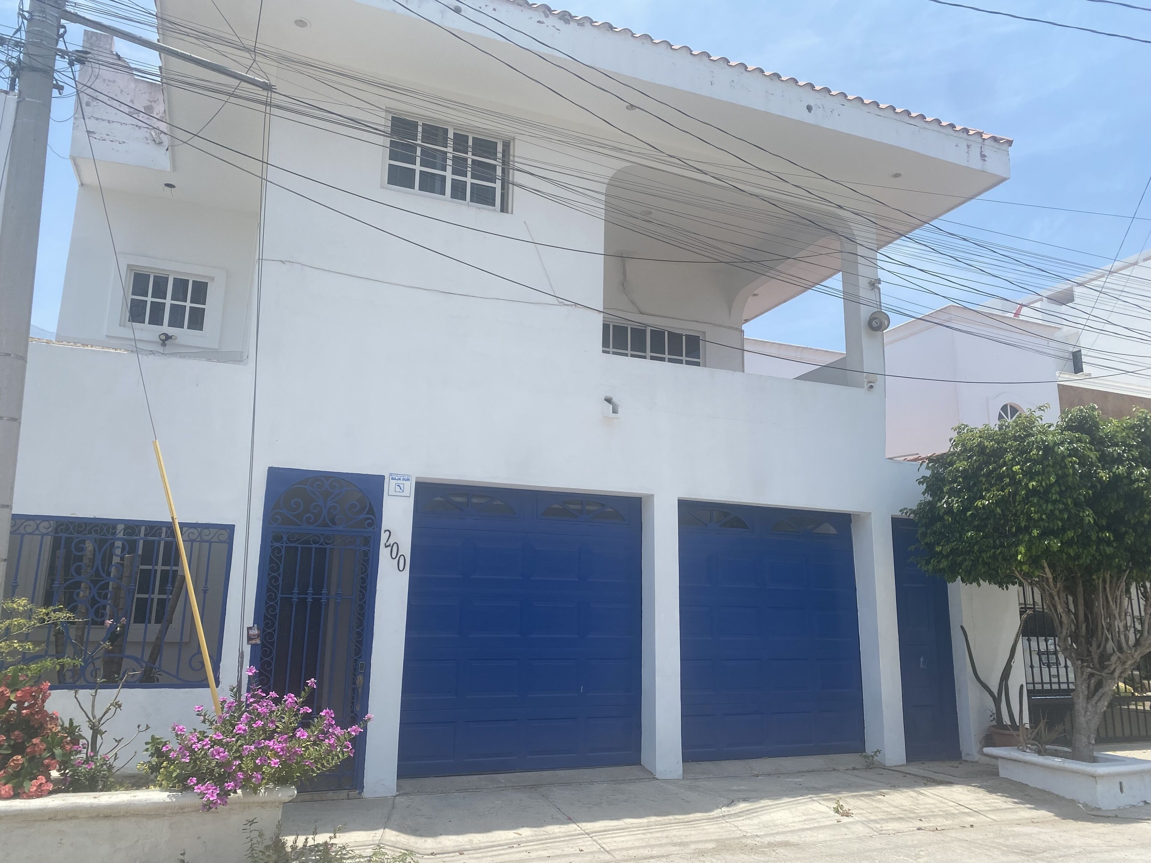 Un edificio de dos plantas con fachada blanca, dos puertas de garaje azules y un pequeño balcón.