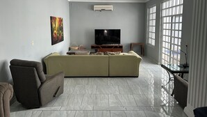 Una sala de estar con un sofá grande, un televisor y una ventana con persianas.