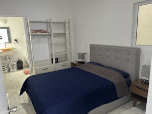 A bedroom with a bed, a nightstand, a wardrobe, and a bathroom visible through an open door.