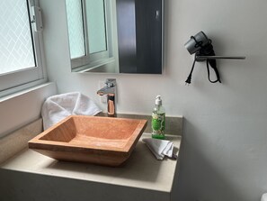 A bathroom with a wooden basin, a towel, a bottle of hand soap, and a mirror.