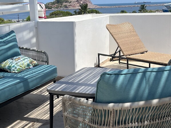 A balcony with a wicker chair and a sofa, both with blue cushions.