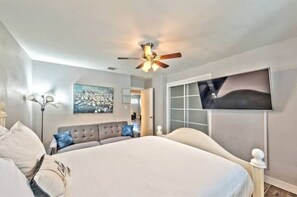 Relax in a spacious bedroom with a large bed, ceiling fan, and flat-screen TV, offering a view of the outdoors.