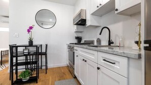 A modern kitchen with white cabinets, a black countertop, a round mirror, and a dining area with a black table and chairs. - Modern Studio in Los Angeles (Los Angeles)