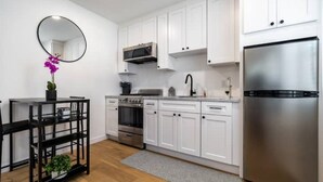 A modern kitchen with white cabinets, stainless steel appliances, and a black dining table with chairs. - Modern Studio in Los Angeles (Los Angeles)