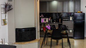 A modern kitchen with dark cabinets, a black refrigerator, and a dining area with a glass table and chairs. - Black suites 1 (Chania)