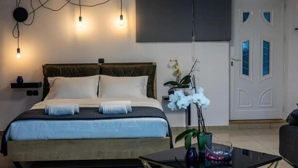 A bedroom with a bed, bedside table, and a potted orchid. - Black suites 1 (Chania)