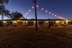 A building with a row of windows, a covered patio area with tables and chairs, and string lights above. - #2 The Point - Double Bed Room (adjoining) (Hot Springs)