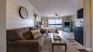 A living room with a sofa, coffee table, and a view through a large window. - #7 Main Channel - King Room (adjoining) (Hot Springs)