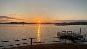 Een zonsondergang boven een kalm meer, met een steiger en een hekwerk op de voorgrond.