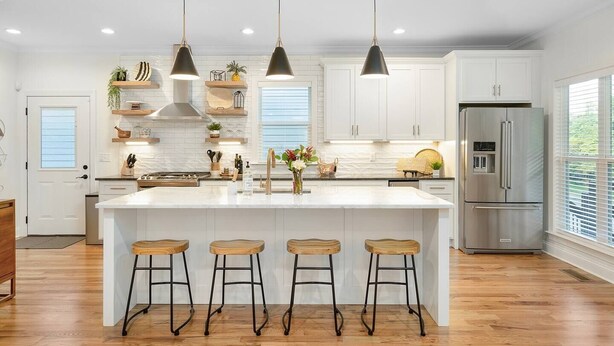 Una cucina moderna con mobili bianchi, una grande isola con sgabelli, illuminazione a sospensione e un frigorifero in acciaio inossidabile.
