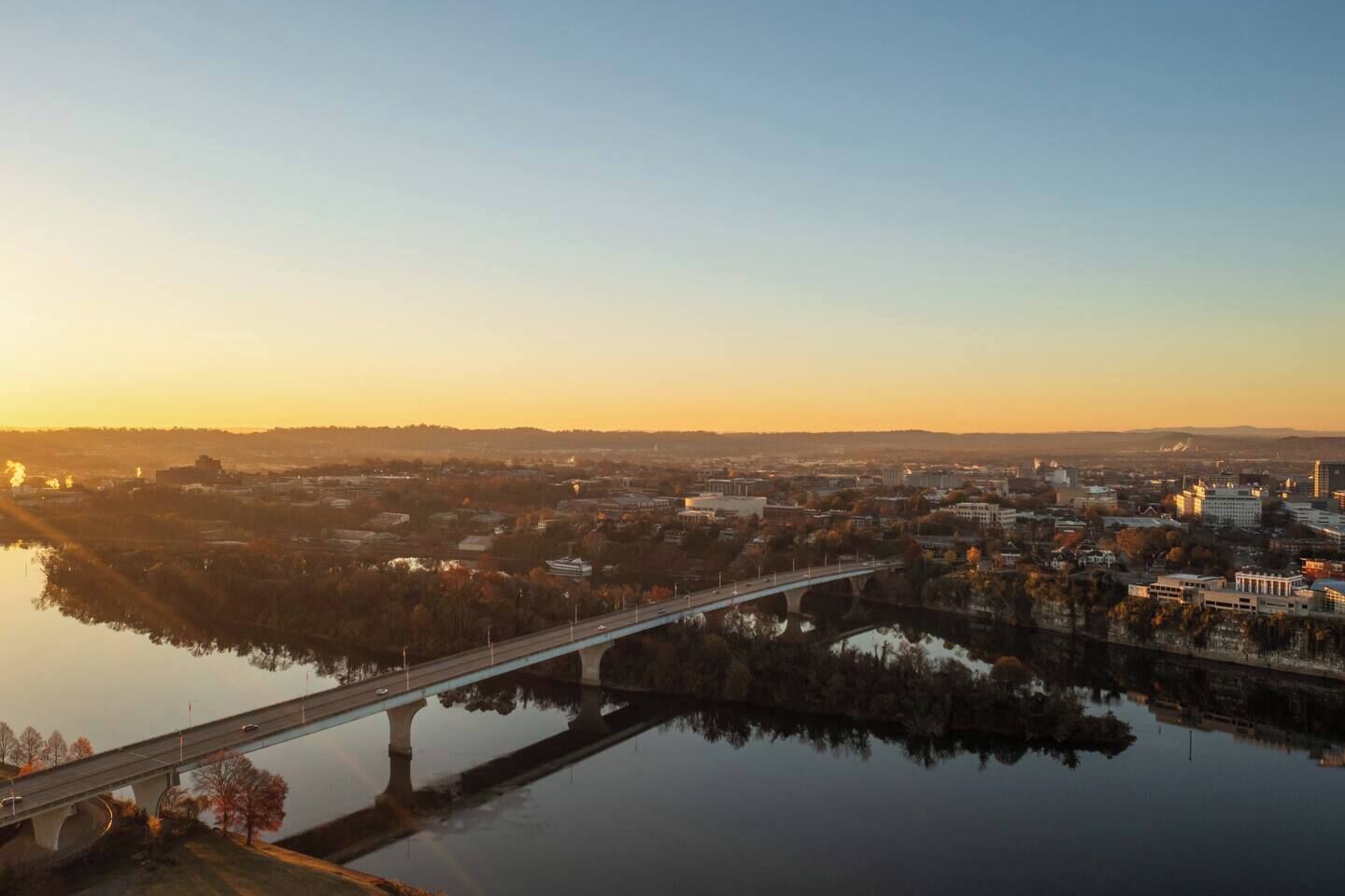 A cityscape with a bridge over a calm river, surrounded by buildings and trees.