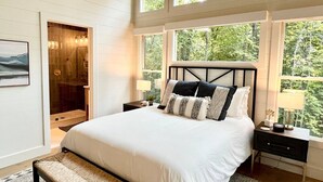 A bedroom with a large bed, a walk-in closet, and a view of the outdoors through large windows.