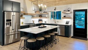 A modern kitchen with a central island, stainless steel appliances, and a wooden ceiling.