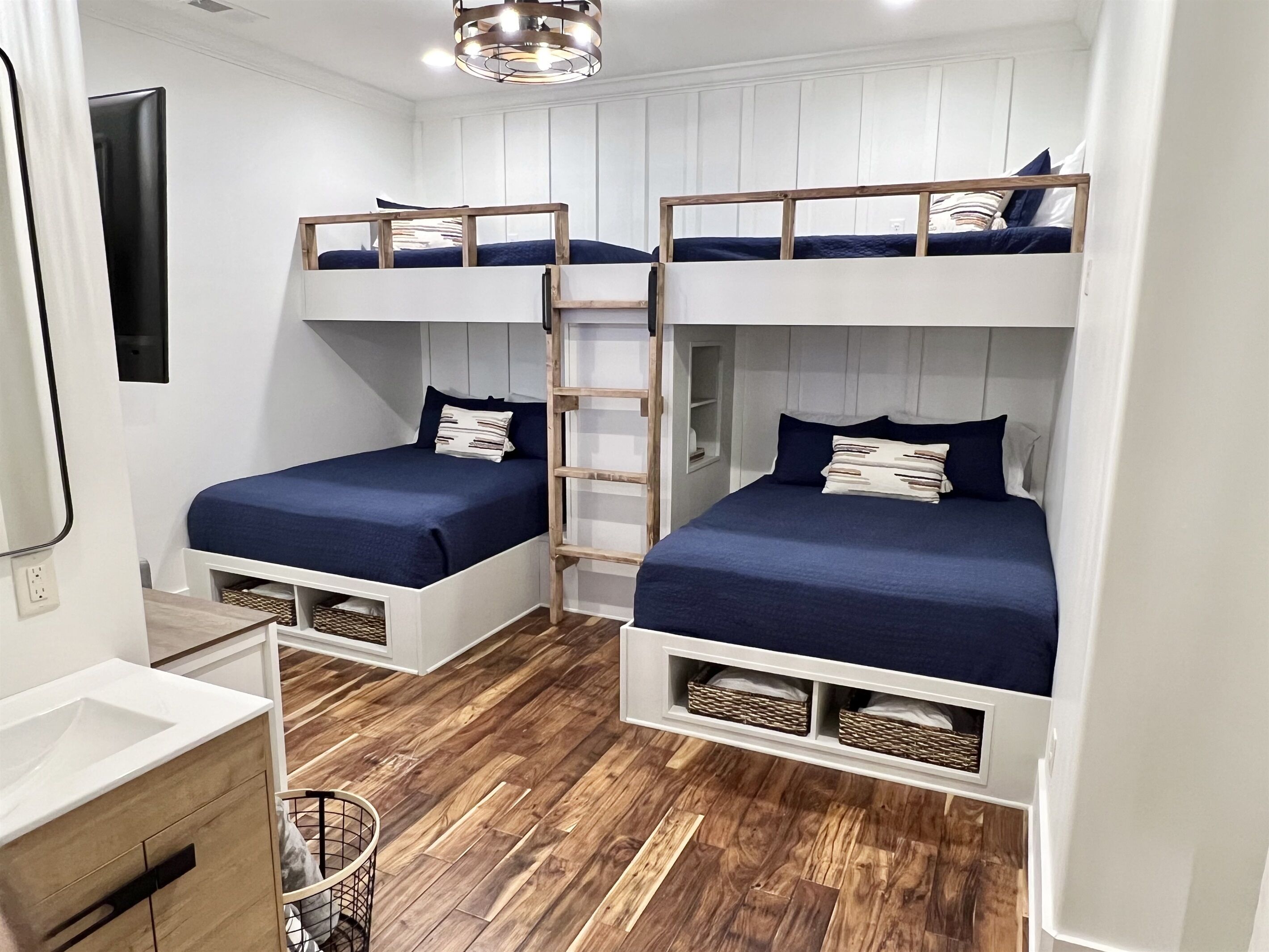 Una habitación pequeña con literas, piso de madera, almacenamiento integrado y una kitchenette.