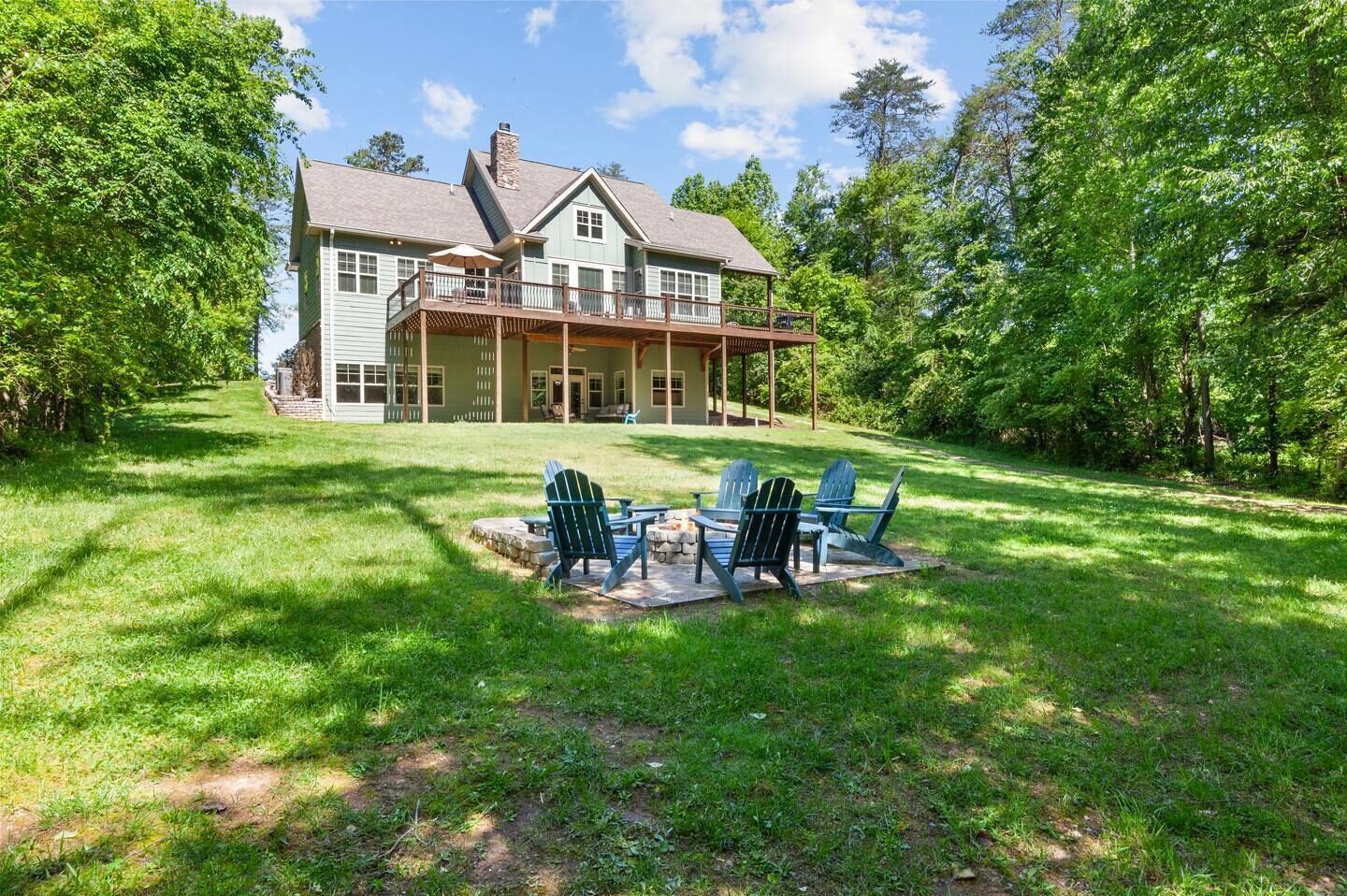 A two-story house with a covered porch and a patio area with Adirondack chairs.