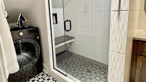 A compact bathroom with a glass-enclosed shower, a washing machine, and a tiled floor. - Lofty Dream | Stylish Northshore Loft Stay (Chattanooga)