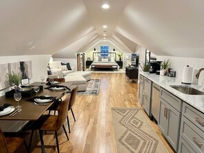 A modern loft-style bedroom with a large bed, a desk, and a dining area.