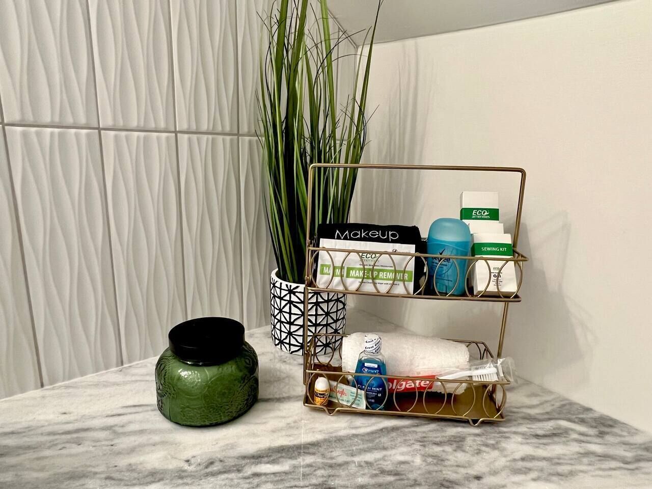 Un plan de travail en marbre agrémenté d’un organiseur de maquillage, d’un vase vert et d’une grande plante.