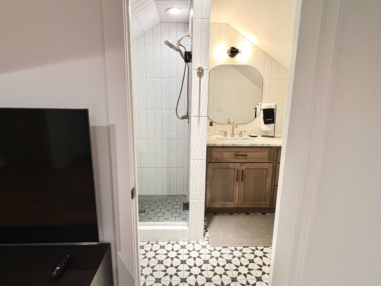 A bathroom with a shower, a mirror, a sink, and a television.
