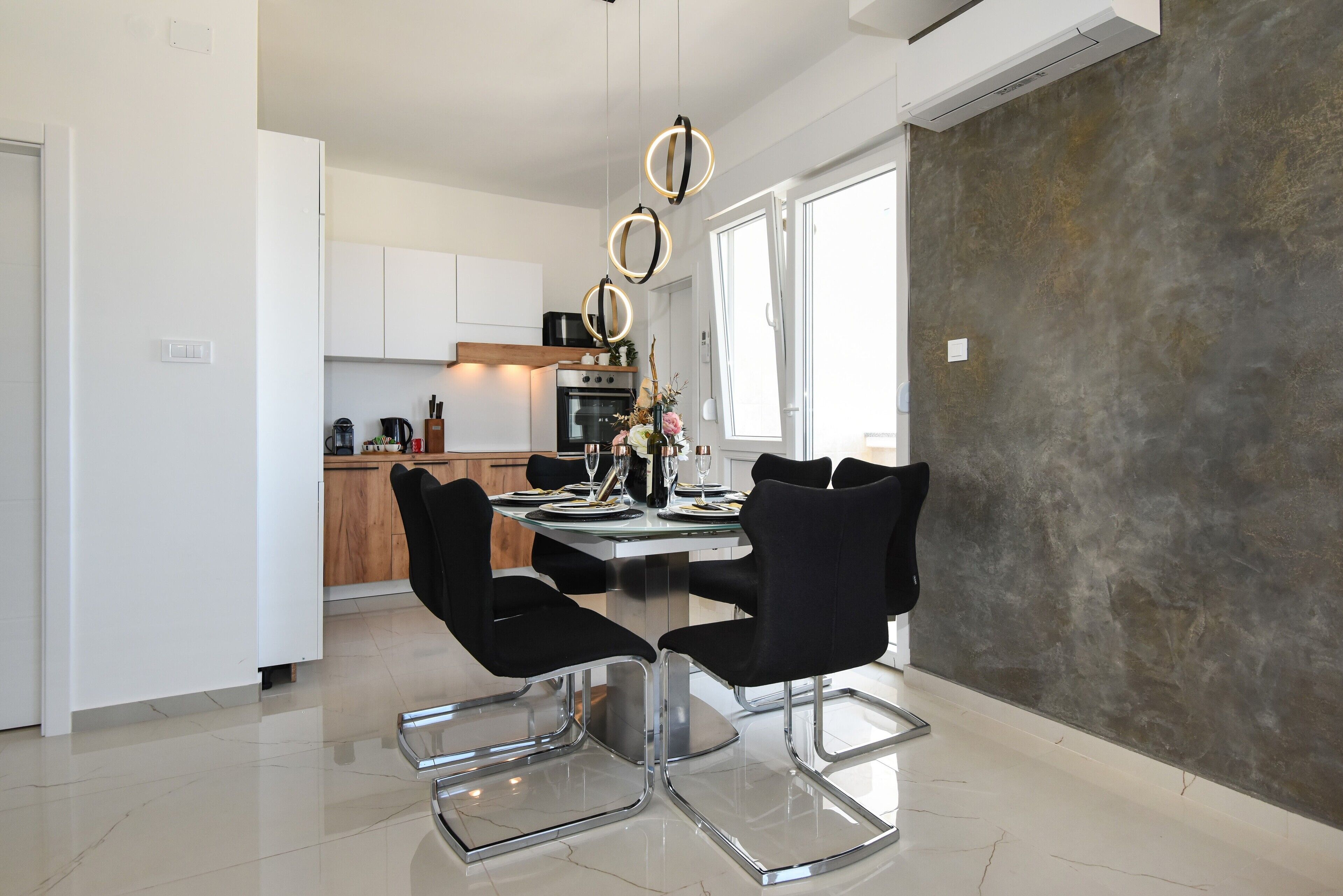 Un espace repas moderne avec une table en verre, des chaises noires et une cuisine en arrière-plan.