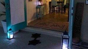 A doorway leading into a room with a dining table and chairs, a small table with a lamp, and a door with a mat. - Quaint Coastal Pool Home Oasis Florida Space Coast, by Beach&Space Coast Stadium (Melbourne)
