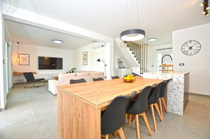 A modern kitchen with a wooden dining table, black chairs, and a marble island. - Villa 5H (Kanfanar)