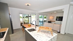 A modern kitchen with a marble island, a dining area with a wooden table, and a living area with a sofa and TV. - Villa 5H (Kanfanar)