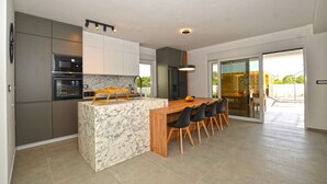 A modern kitchen with a marble island, built-in appliances, and a dining area with chairs. - Villa 5H (Kanfanar)