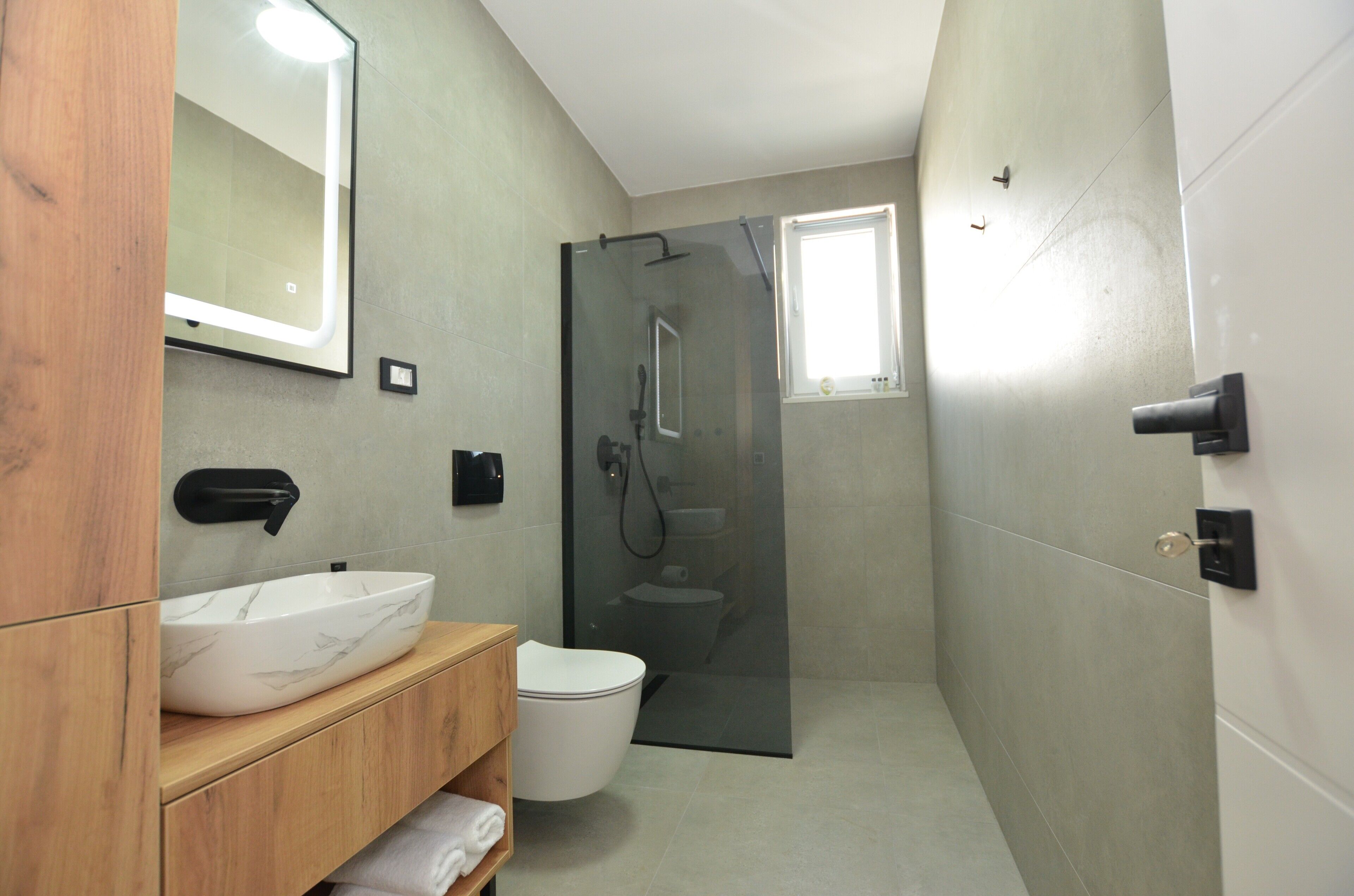Ein modernes Badezimmer mit einer Duschkabine aus Glas, einer weißen Toilette und einem Holzwaschtisch mit Marmorbecken.