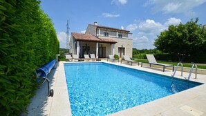 A rectangular swimming pool with a tiled deck, surrounded by a hedge and a building with a sloped roof. - Villa dado (Kanfanar)