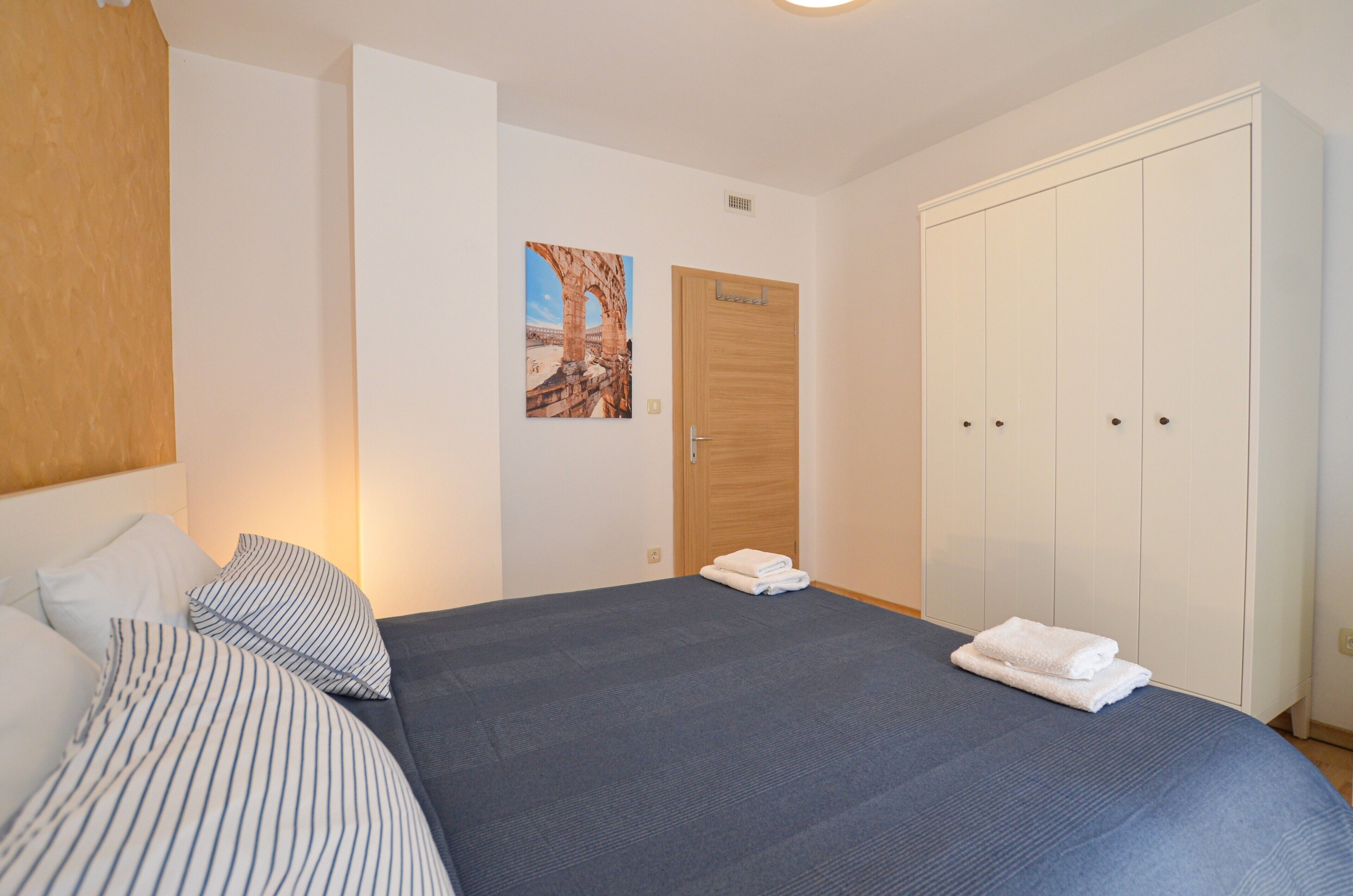 Een slaapkamer met een bed, kussens, een houten deur en een kledingkast.