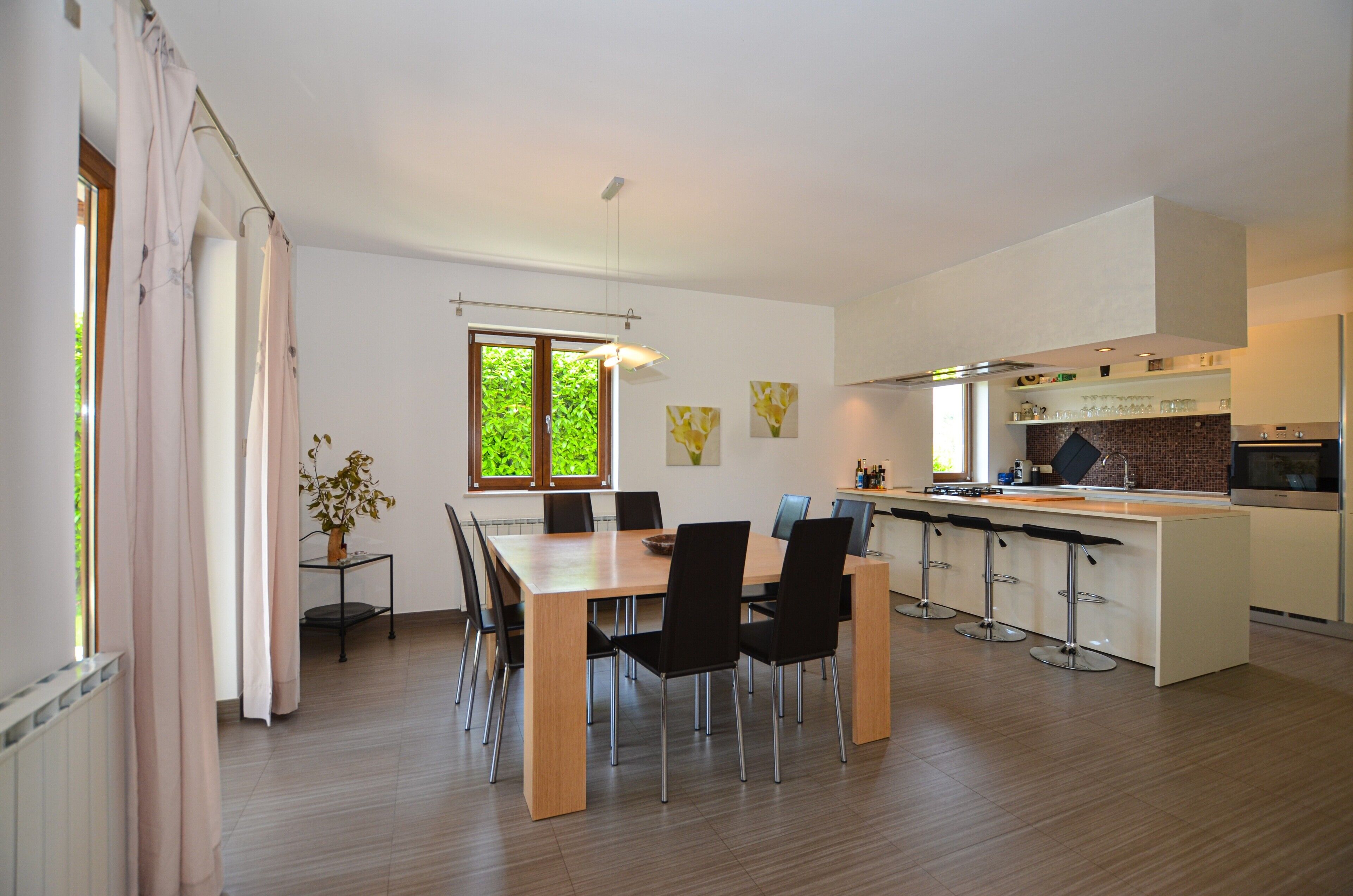 A modern kitchen with a central island, bar stools, and a dining area with a wooden table and chairs.