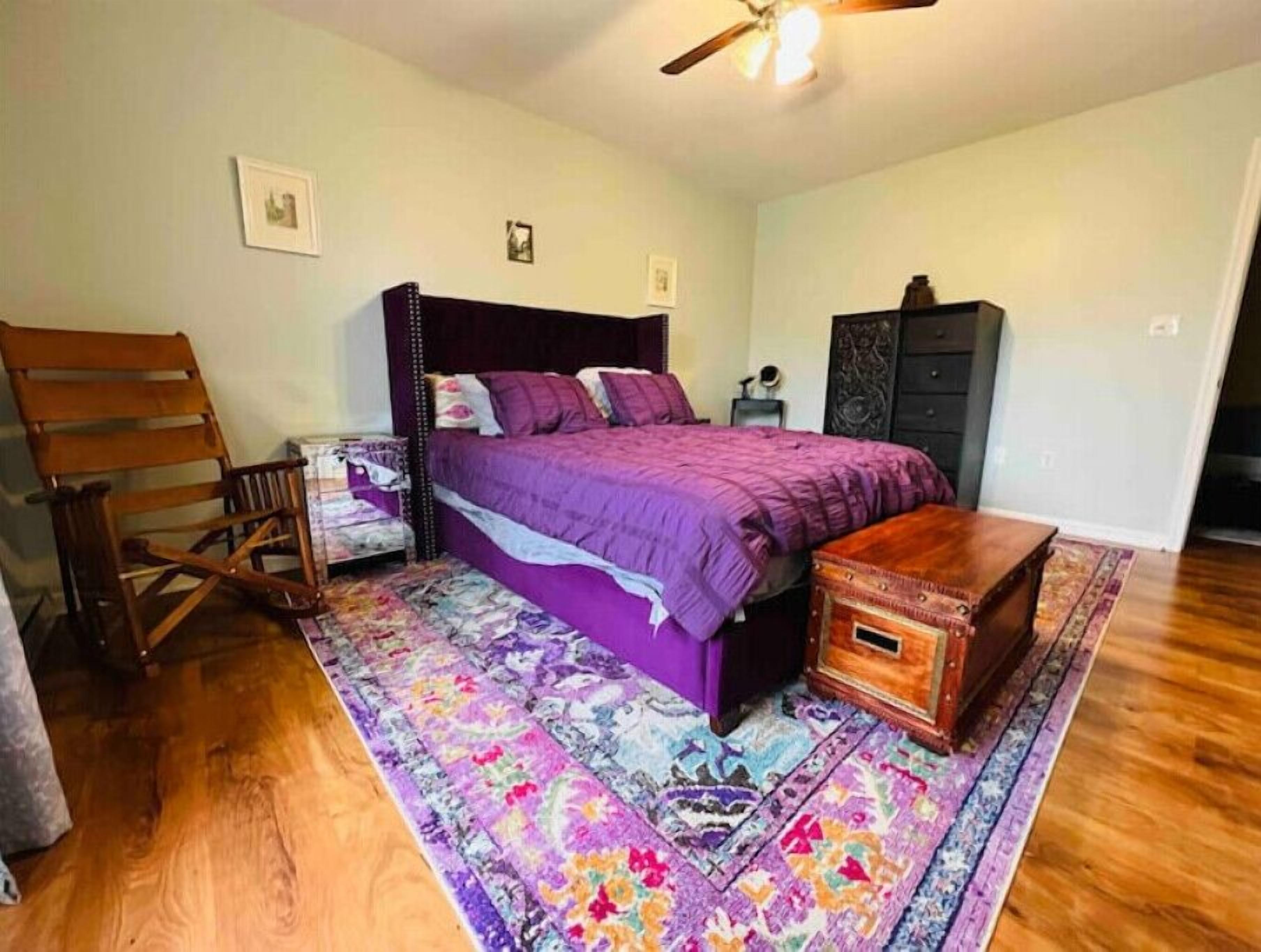 Ein Schlafzimmer mit Bett, Holzstuhl, Nachttisch, Kommode und Deckenventilator.