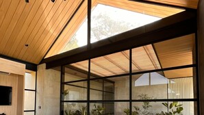 Un soggiorno moderno con un divano componibile bianco, ampie finestre e un soffitto in legno.