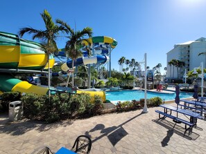 A water park with multiple slides and a pool area, surrounded by palm trees and hotel buildings.