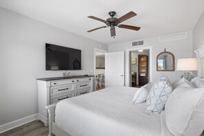Een slaapkamer met een bed, een dressoir, een plafondventilator en een spiegel.