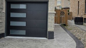 Una casa moderna con puerta de garaje oscura, fachada de piedra y un camino de entrada bien cuidado.