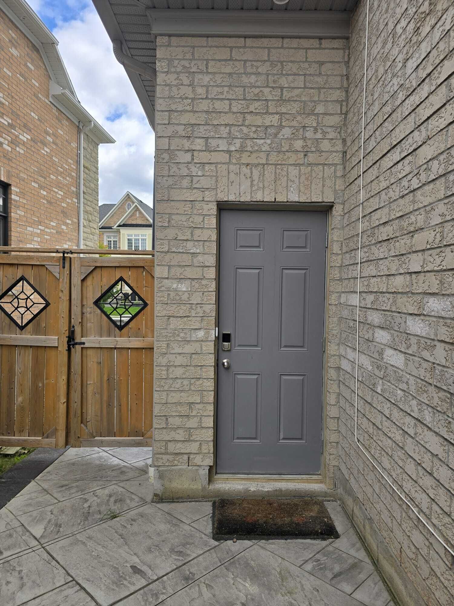 A grey door with a small window, a wooden gate with diamond-shaped glass panels, and a stone wall.