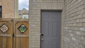 Una puerta gris con un pequeño ventanal, un portón de madera con paneles de vidrio en forma de rombo y un muro de piedra.