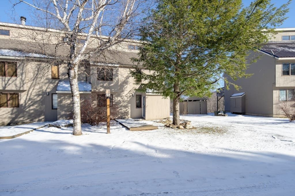 Un edificio residencial con un patio cubierto de nieve, un cobertizo pequeño y un árbol.
