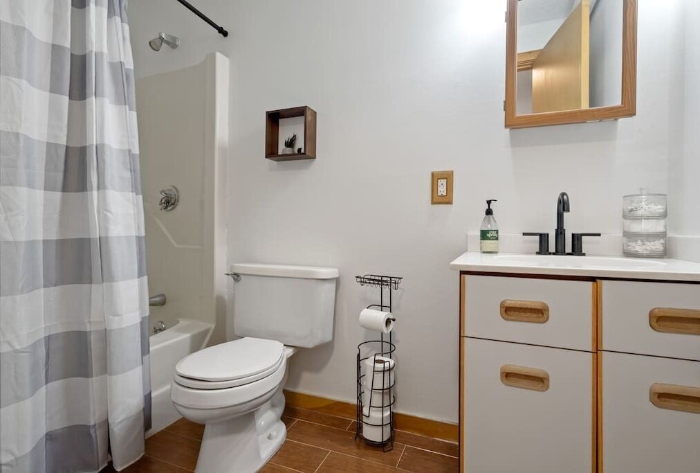 A bathroom with a toilet, shower curtain, sink, and storage cabinet.