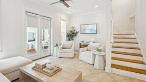 A spacious living room with a white sofa, two armchairs, a coffee table, and a wooden staircase.