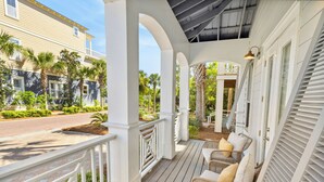 A covered porch with wicker furniture and a view of a street and neighboring buildings.