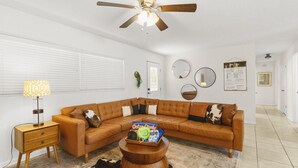 A living room with a brown leather sectional sofa, a wooden coffee table, a lamp, and a ceiling fan. - The Gator Getaway- Huge Backyard (Gainesville)