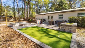 A backyard with a putting green, stone seating, and a patio area. - The Gator Getaway- Huge Backyard (Gainesville)