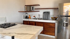 Una cocina con encimera de mármol, armarios de madera, estufa a gas, microondas, licuadora, fregadero y refrigerador de acero inoxidable.