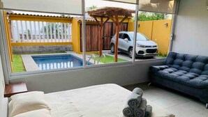 Un dormitorio con cama, vista a una piscina, un sofá y un coche estacionado afuera.