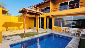 A pool area with a pergola, outdoor seating, and a two-story building with large windows.