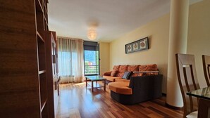 A living room with a sofa, a coffee table, and a chair. There is a window with curtains and a door leading outside. - The Llaneces Lookout 24A02 by R2R Consulting (Arenas de Cabrales)